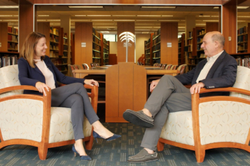 Two people sit in chairs facing each other in a library