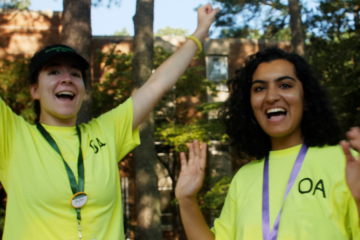 Two people in bright yellow T-shirts raise their arms and cheer