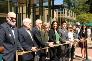 People standing in a line prepare to cut a large ribbon in front of a building