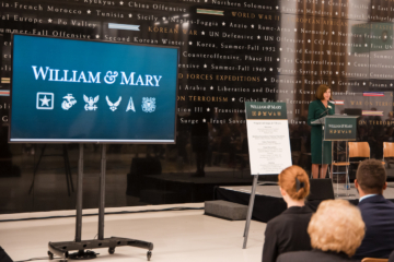 A person speaks at a podium next to a screen that says William & Mary