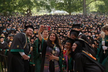 People wearing caps and gowns take a photo in front of a large crowd