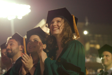 People wearing academic regalia stand and applaud