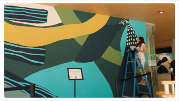A person stands on a ladder and paints a wall