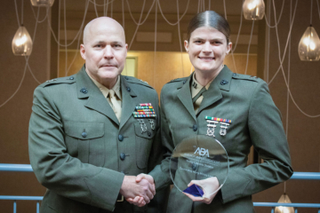 A person in a military uniform accepts an award from another person