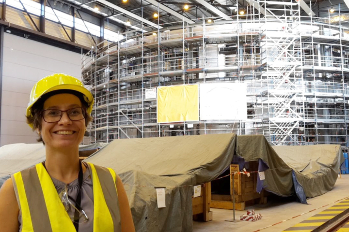 Associate Professor Saskia Mordijck at ITER in Southern France, where several international members are collaborating to build the world's largest tokamak. She is wearing a yellow vest and a helmet and posing in front of a cryostat.