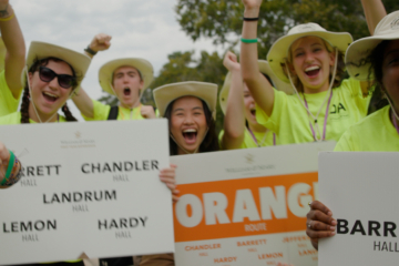 People in neon yellow shirts cheer and hold signs with residence hall names on them