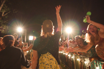 A person waves while walking through a crowd of people at night