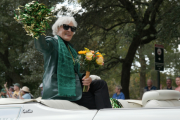 Glenn Close holds flowers and waves from the back of a car
