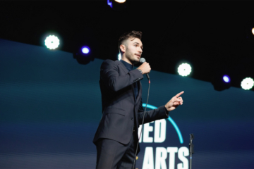 A person stands on a stage and speaks into a microphone