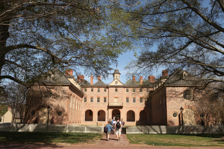 People walk toward a large, brick building surrounded by trees.