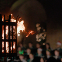 A fire blazes in a torch while a choir sings in the background.