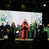 People wearing academic regalia stand on a stage.