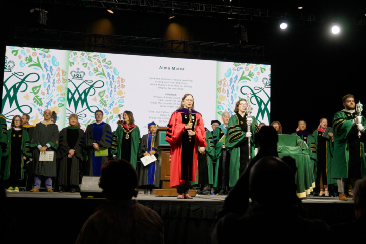 People wearing academic regalia stand on a stage.