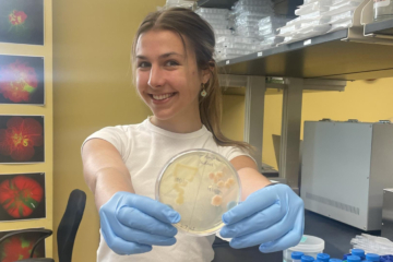 A person holds a Petri dish while wearing gloves in a lab.