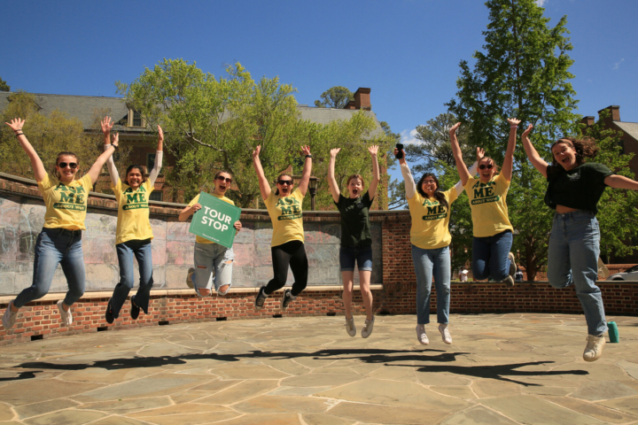 Eight people wearing "Ask Me About W&M" shirts jump in the air.