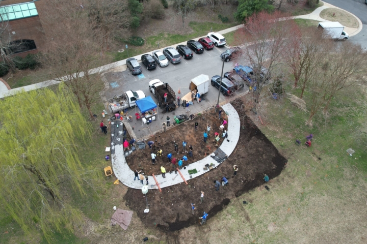 An aerial shot of Melissa's Meadow, with multiple people standing on patches of dirt, with a tent and various trucks and cars in the parking lot.