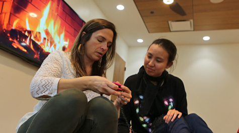 Two people sit on a floor and work on a knitting project