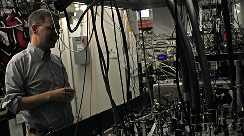 Seth Aubin, associate professor of physics at William & 玛丽, stands in front of a table of lenses, mirrors and other optics that his team uses to manipulate light to cool rubidium and potassium atoms. 