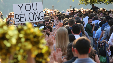 A sign saying "You Belong" is held up among a large crowd outside of the Wren Building