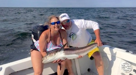 Two people on a boat hold a large fish.