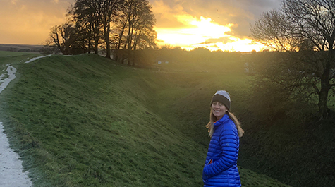 Carrie Dolan stands in front of a sunset in a remote rural landscape. 