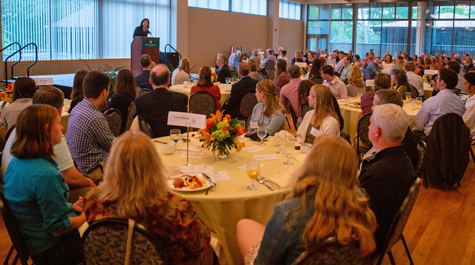 Katherine Rowe speaks to families sitting at tables in a large room
