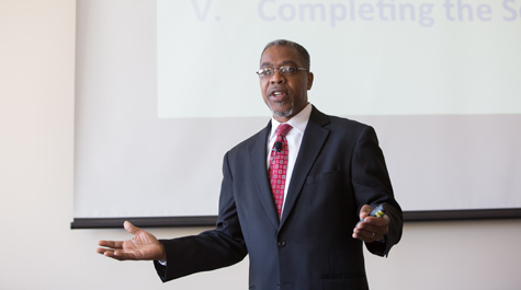 Chris Lee speaks while standing in front of a screen