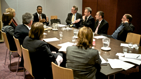 Chris Lee sits at the head of a table and talks to others in a business meeting