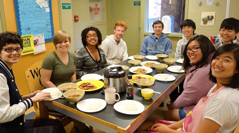 Students sitting around a dinner table together smile at the camera