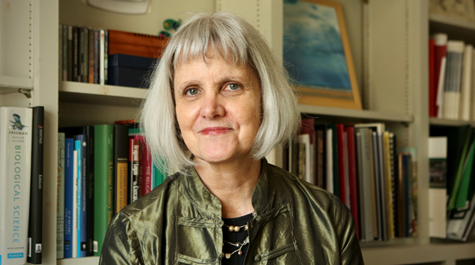 Kate Conley wears a green jacket and stands in front of a bookcase