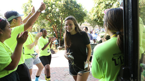 A new student enters her dorm as orientation aides on each side of the door applaud