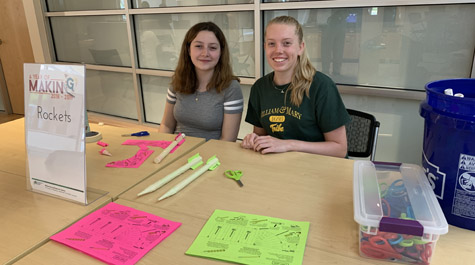 Two people sit at a table with crafting materials and a sign that says A Year of Making - Rockets