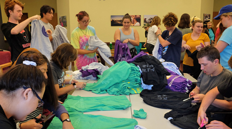 Students work on cutting up and tying together shirts around a table