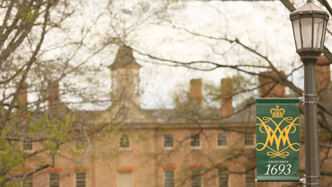 A banner with the William & 玛丽 cypher and 1693 on it hangs on a lightpole in front of the Wren Building