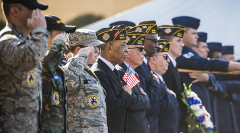 Veterans and military members in uniform salute and hold a flag