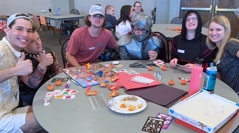 People sitting around a table, some wearing costumes, smile at the camera