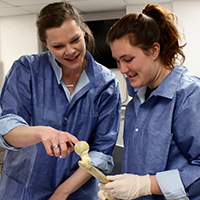 William & 玛丽 student Laura Anderson is seen working in the Anatomy Lab, instructing a fellow student about the structures within an actual human bone. 