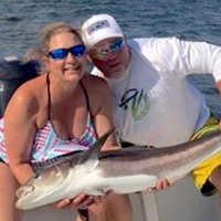 Two people on a boat hold a large fish.
