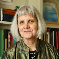 Kate Conley wears a green jacket and stands in front of a bookcase