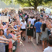 Students walk through a line of people giving them high-fives and holding signs