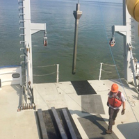 A man in hard hat and orange vest walks on the back of a boat