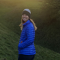 Carrie Dolan stands in front of a sunset in a remote rural landscape.