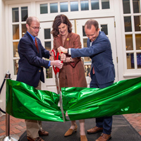 Three people use large scissors to cut a giant, green ribbon
