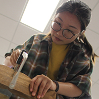 A William & 玛丽 student saws a piece of wood for a sculpture design