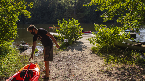 A student wearing a mask pulls a canoe toward Lake Matoaka