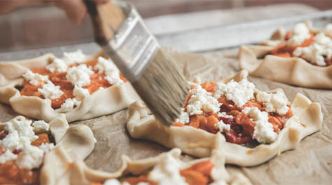 A close-up of a brush spreading something on pastries