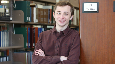 Justin Estreicher stands beside stacks in a library