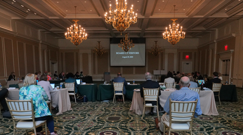 People sit in chairs and at tables in a large room with elaborate chandeliers