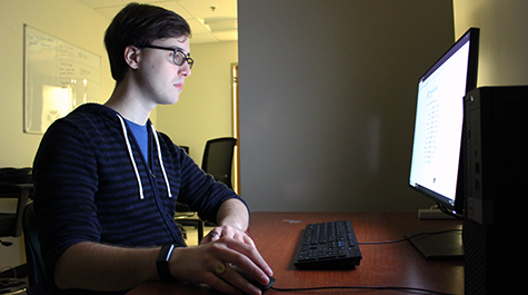 Garret Walker, class of 2019, sits in front of a computer in the lab that he manages