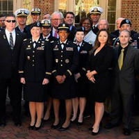 People in different military uniforms pose for a photo together in front of a brick building